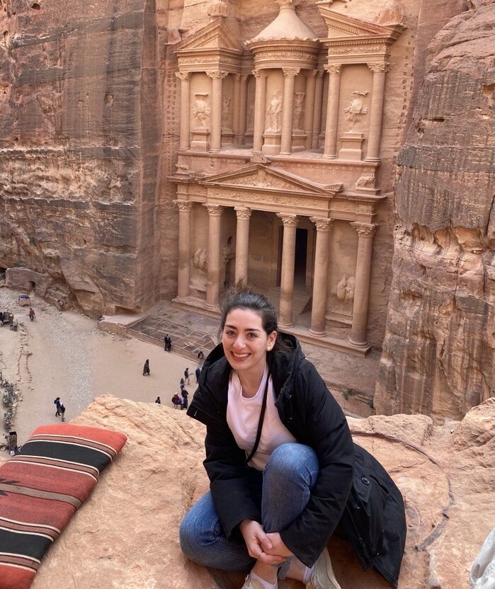 Serena Tohmé smiling in front of the ancient rock-cut facade of al-khazneh in Petra, Jordan.