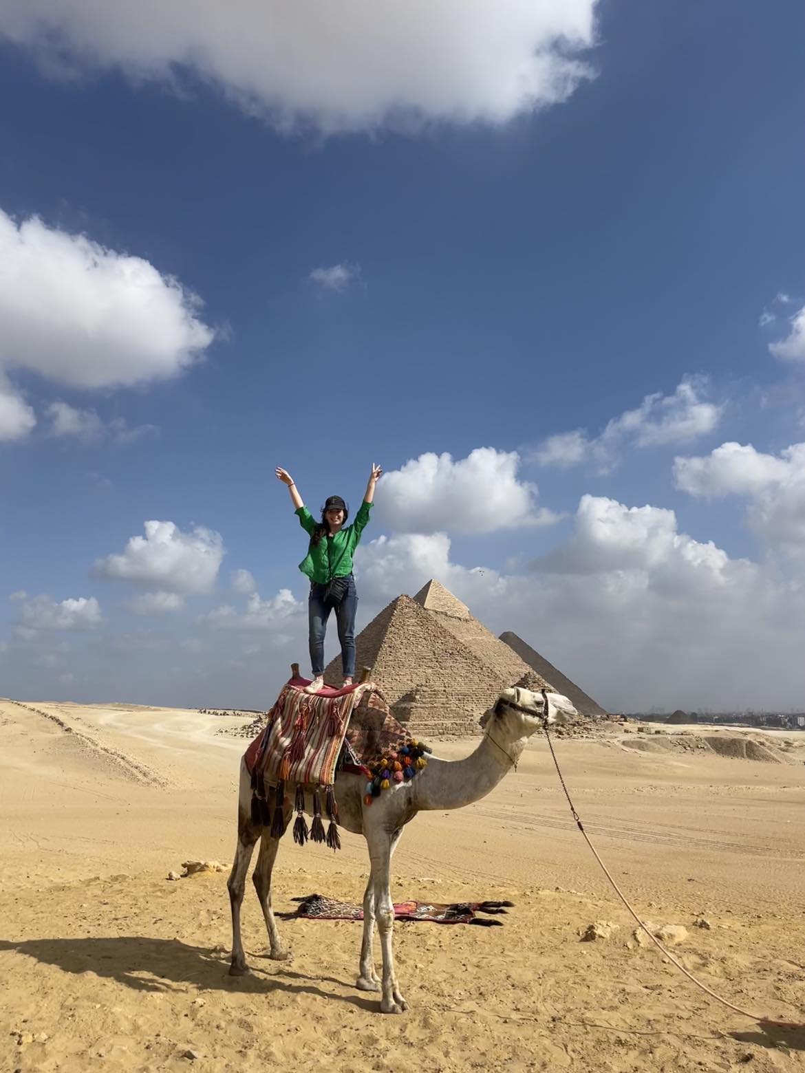 Serena Tohmé, a woman, riding a camel in front of the pyramids.