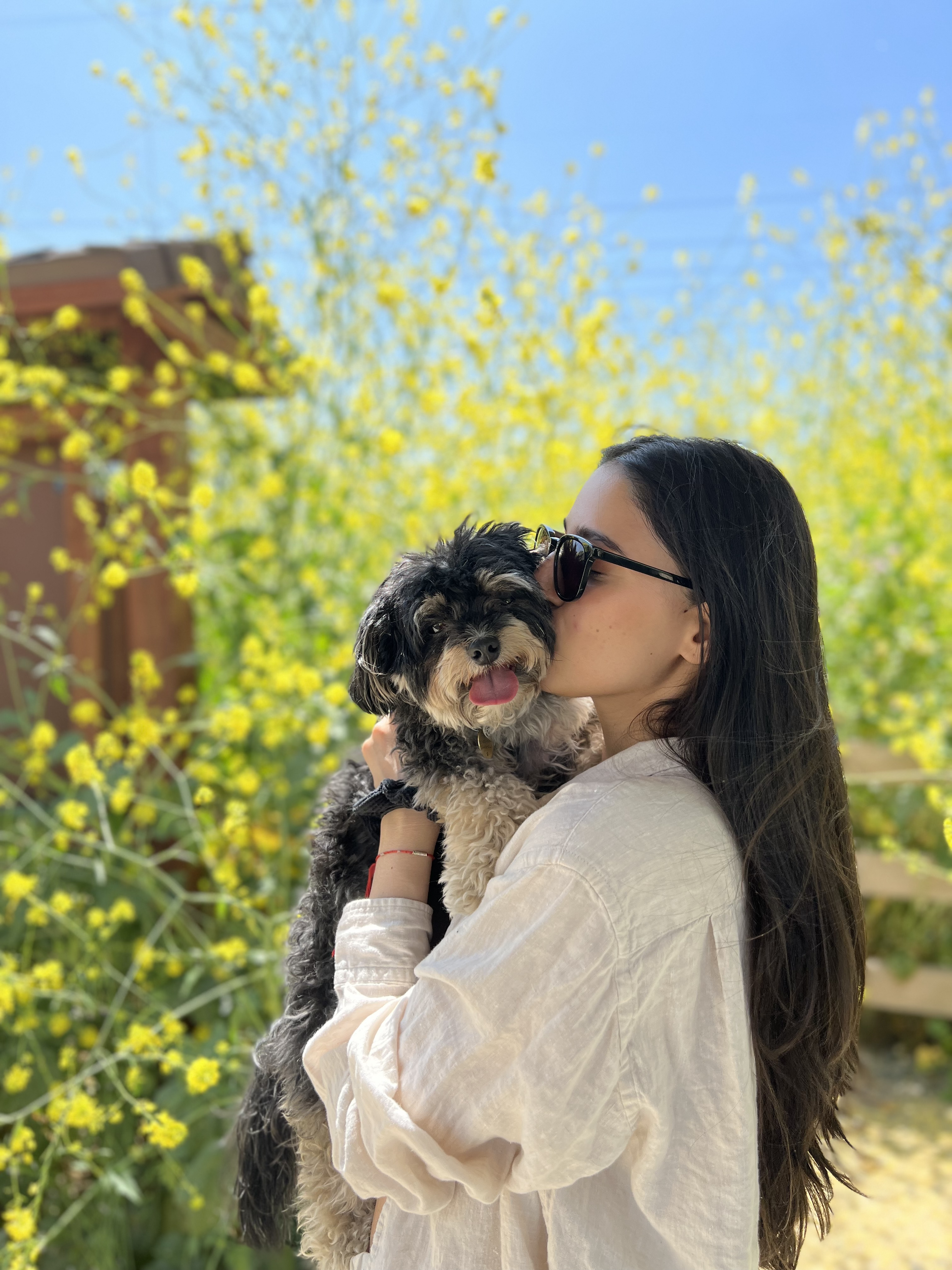 Jasmine Bains hugs a dog in front of a tree on a sunny day.