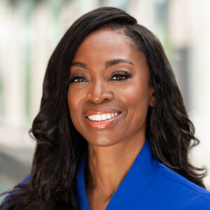 Headshot of a smiling woman with dark hair wearing a blue blazer.